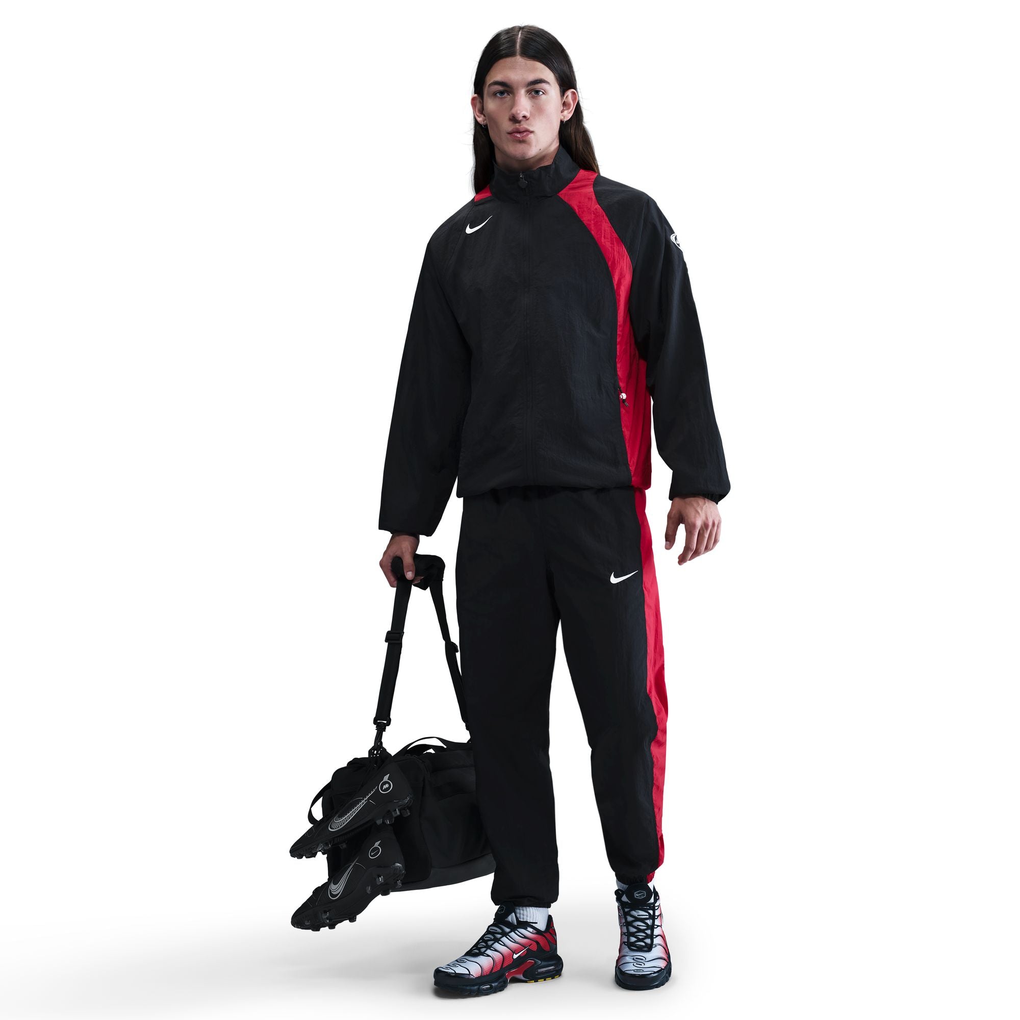Person wearing a black and red Nike tracksuit holding a black bag on a white background