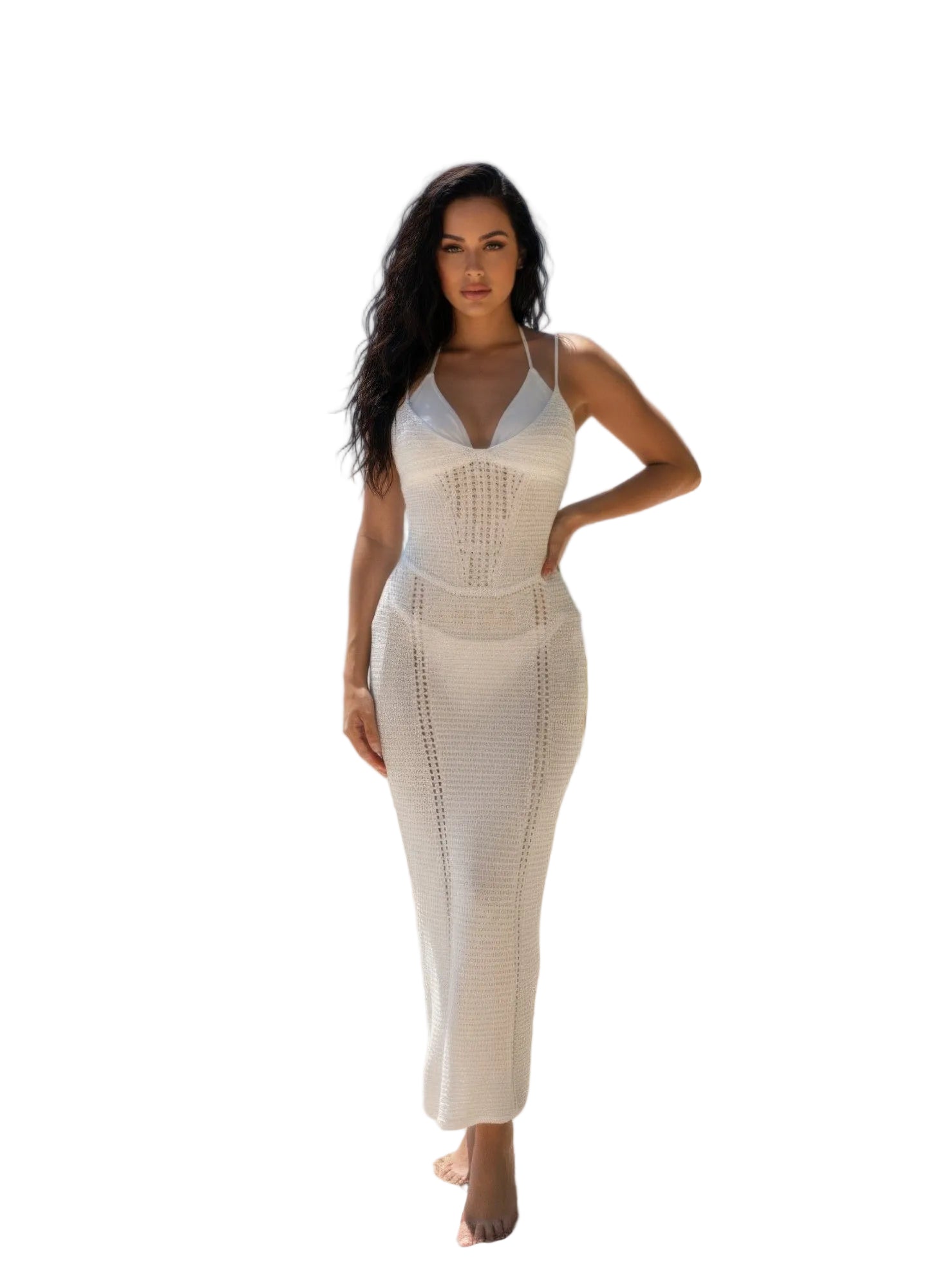 Woman in a white dress standing on a beach with palm leaves and blue sky.