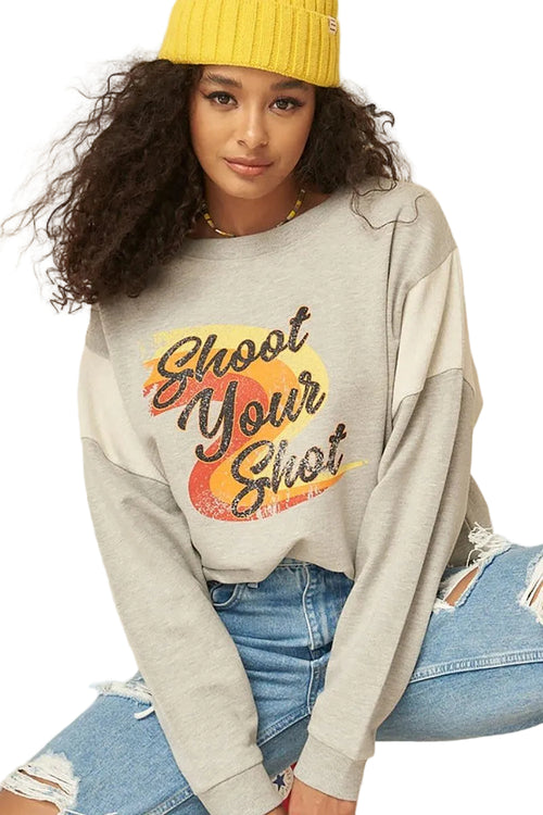 Person wearing a gray sweatshirt with 'Shoot Your Shot' text, yellow beanie, and blue jeans on a beige background