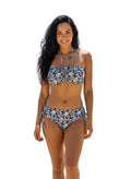 Woman in a floral bikini standing on a beach with clear blue sky and ocean.