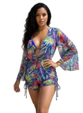 Woman in a colorful floral cover-up standing on a beach with palm trees in the background