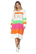 Woman wearing a colorful striped dress with 'PEACE' text, standing against a wooden wall.