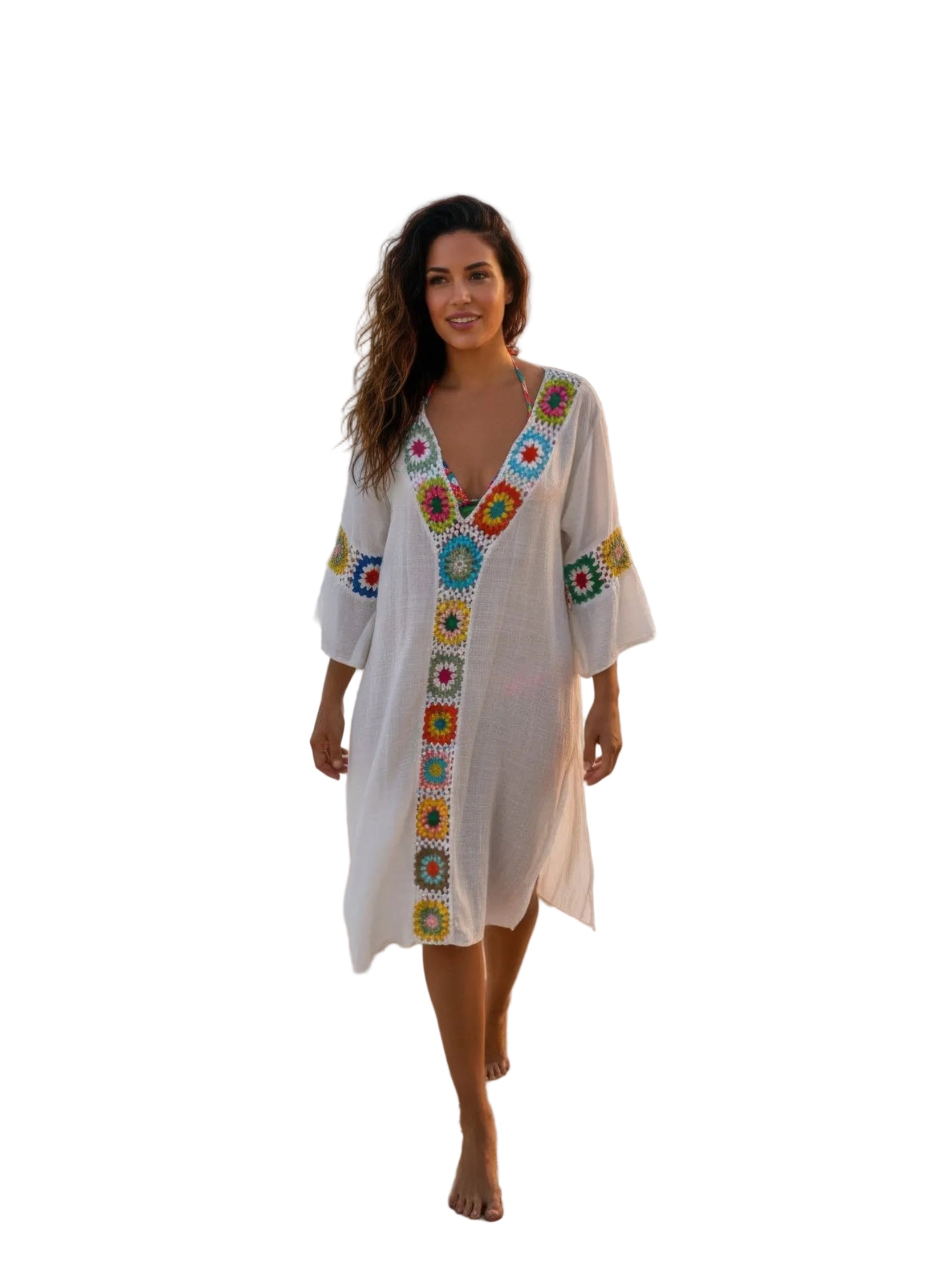 Woman in a colorful beach cover-up standing on a sandy beach with ocean and sunset in the background