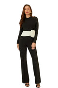 Woman in a black outfit with a white belt and floral detail standing in an elegant interior setting.