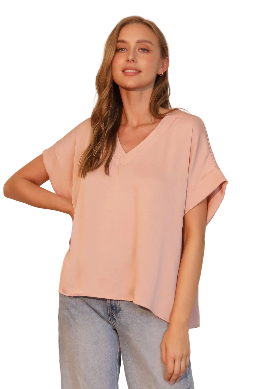 Woman wearing a light pink blouse and blue jeans against a neutral background