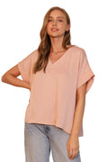 Woman wearing a light pink blouse and blue jeans against a neutral background