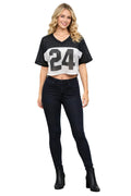 Woman wearing a black and white crop top with the number 24 and black jeans against a white background