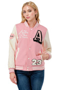 Woman wearing a pink and white varsity jacket with lettering and numbers on a white background
