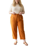 Woman wearing a white top and orange pants standing in a living room.