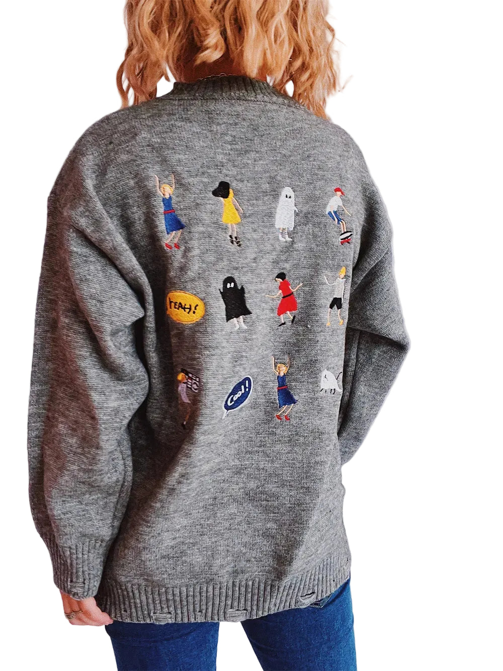 Person wearing a gray sweater with embroidered characters on the back against a plain background