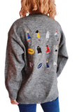 Person wearing a gray sweater with embroidered characters on the back against a plain background