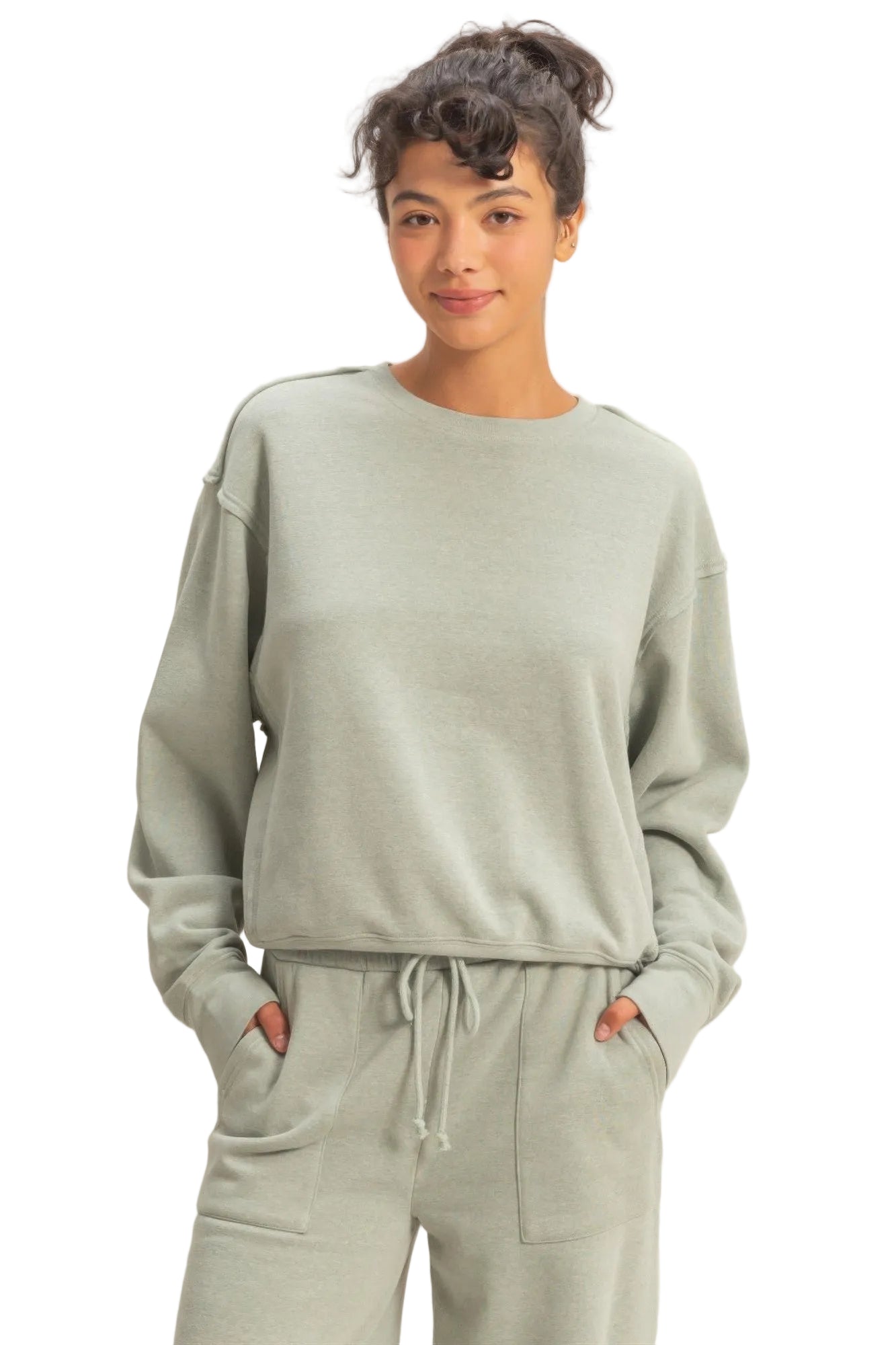 Woman wearing a light green sweatshirt and pants set against a beige background