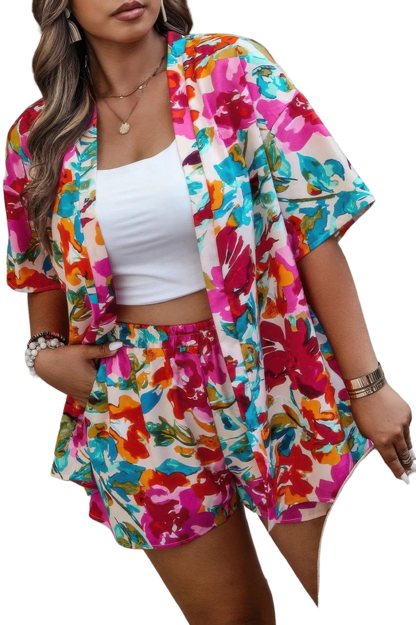 Woman wearing a colorful floral outfit with a white top and shorts, standing against a green curtain.