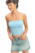 Woman wearing a light blue strapless top and denim skirt against a plain background