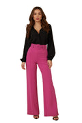 Woman wearing a black blouse and pink pants against a beige background