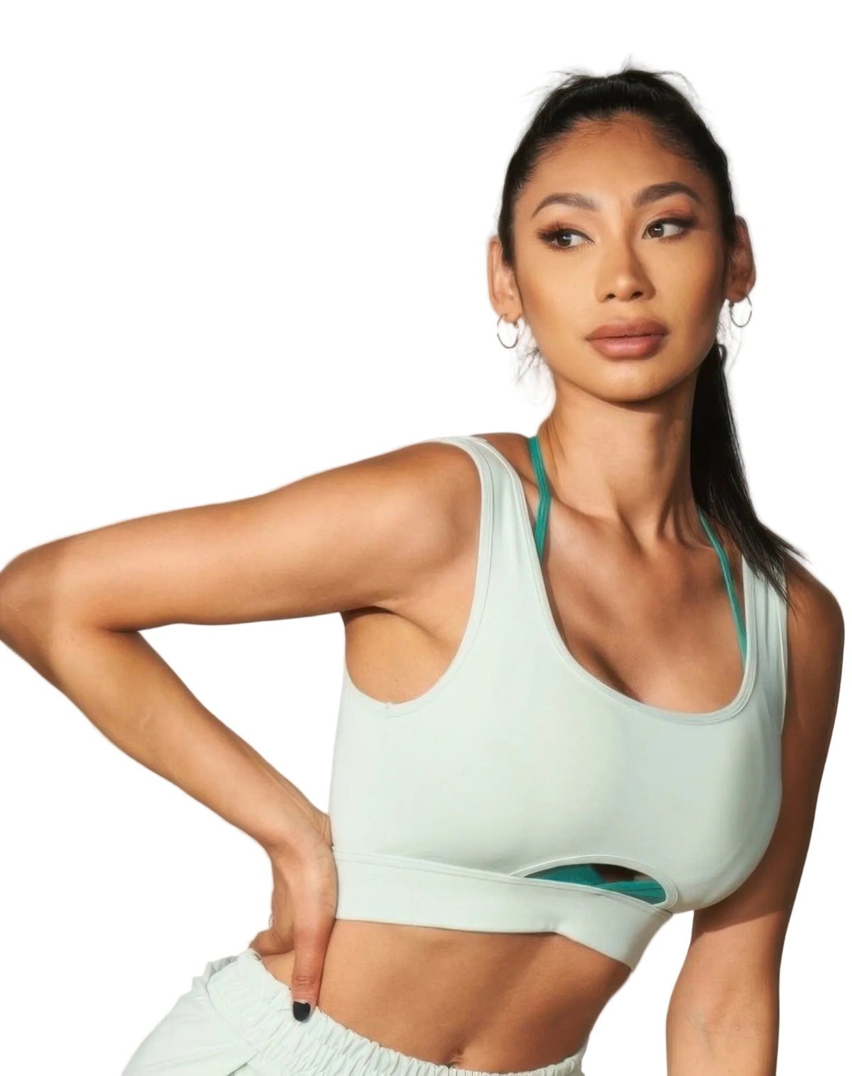 A woman modeling a pale mint green sports bra with teal-green underband and straps, paired with matching light green athletic bottoms, against a plain light gray studio background.