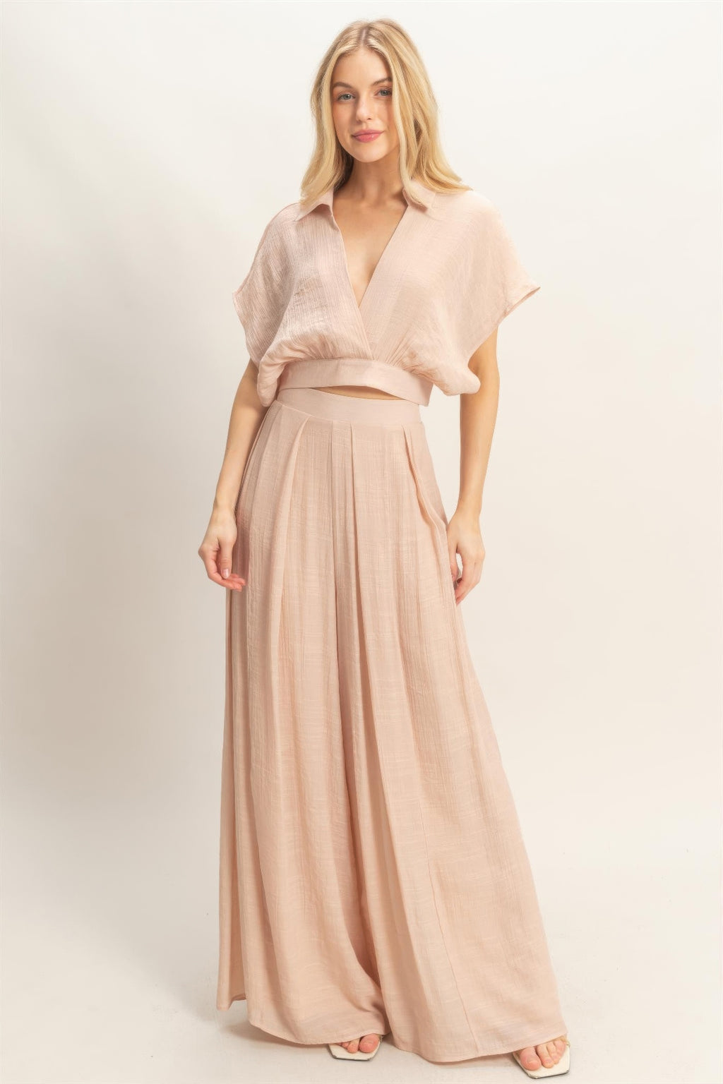 Woman wearing a light pink outfit with a top and long skirt on a white background