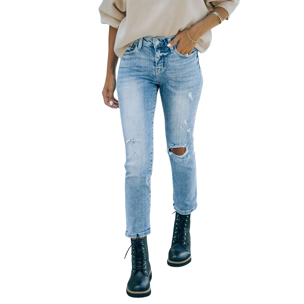 Light blue distressed jeans worn with a beige sweater and black boots on a white background