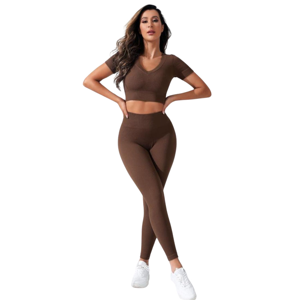 A woman wearing a brown V-neck crop top and high-waistband long active pants, with white sneakers.