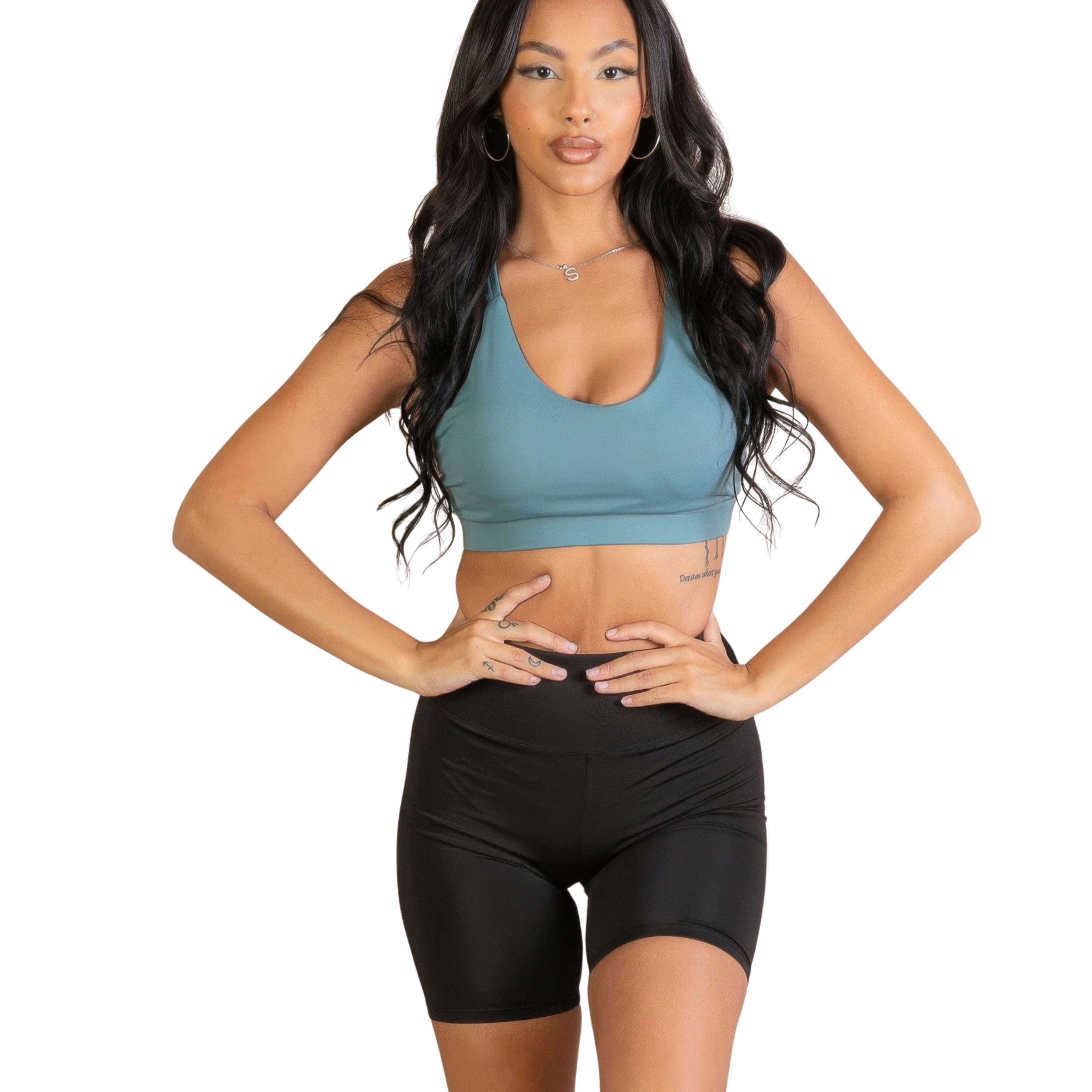 Woman wearing a green sports bra and black shorts on a white background