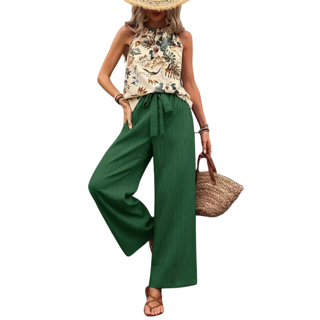 Woman wearing a floral top and green wide-leg pants, holding a straw bag on a white background