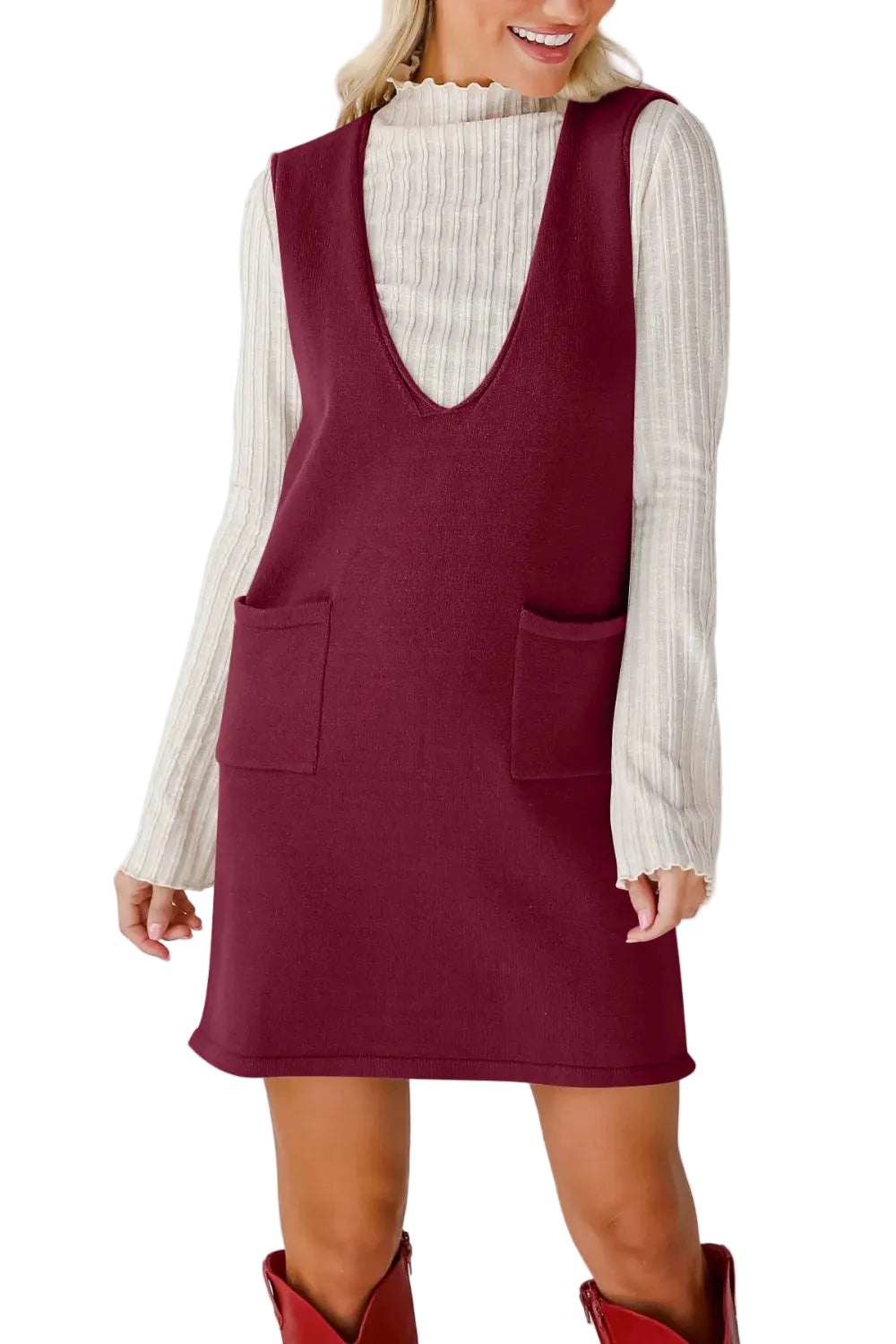 Woman wearing a burgundy sleeveless dress over a white long-sleeve shirt on a plain background