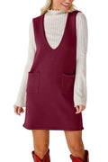 Woman wearing a burgundy sleeveless dress over a white long-sleeve shirt on a plain background