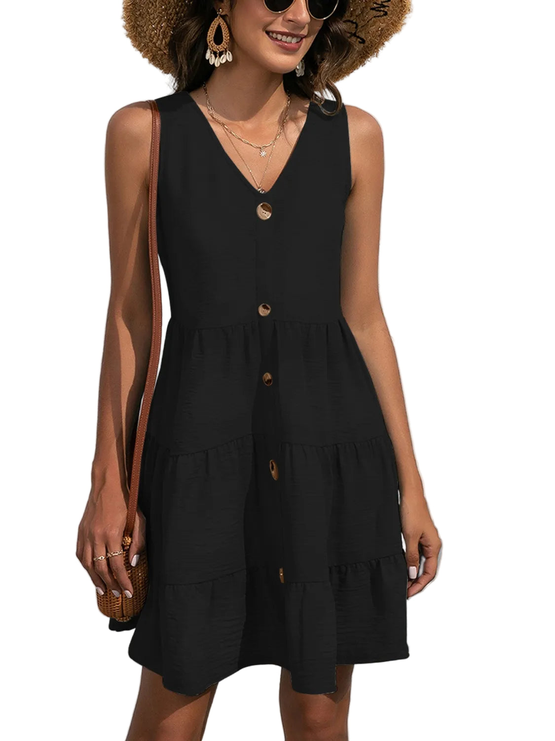 Woman wearing a black sleeveless dress with buttons against a white textured wall.