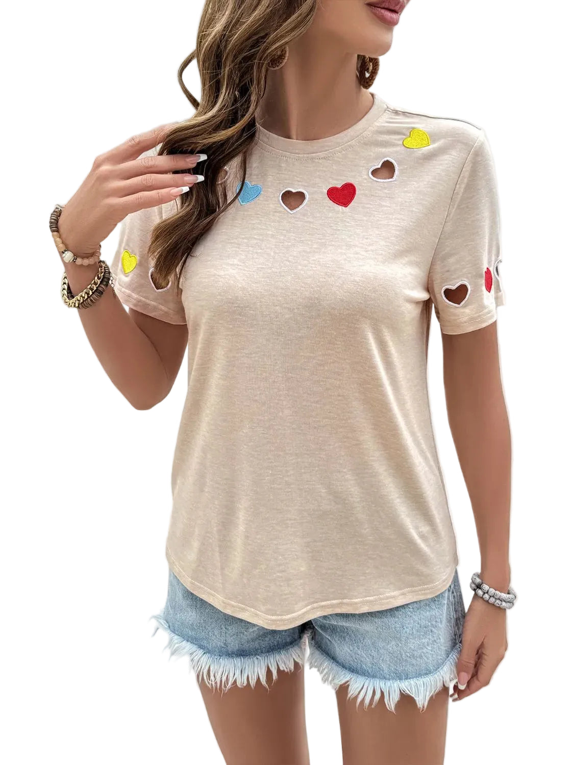 Woman wearing a beige t-shirt with heart designs and denim shorts against a white background