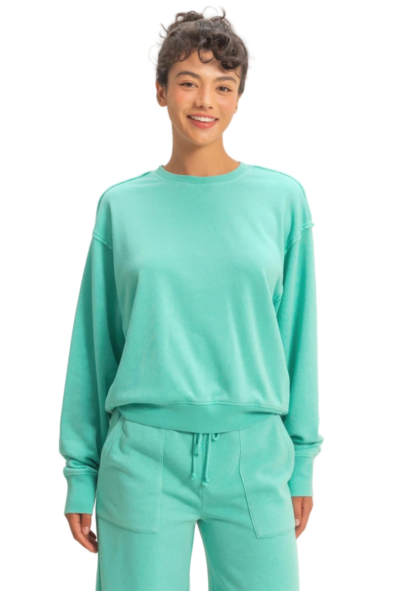 Person wearing a teal sweatshirt and pants on a beige background