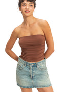Woman wearing a brown strapless top and denim skirt against a plain background