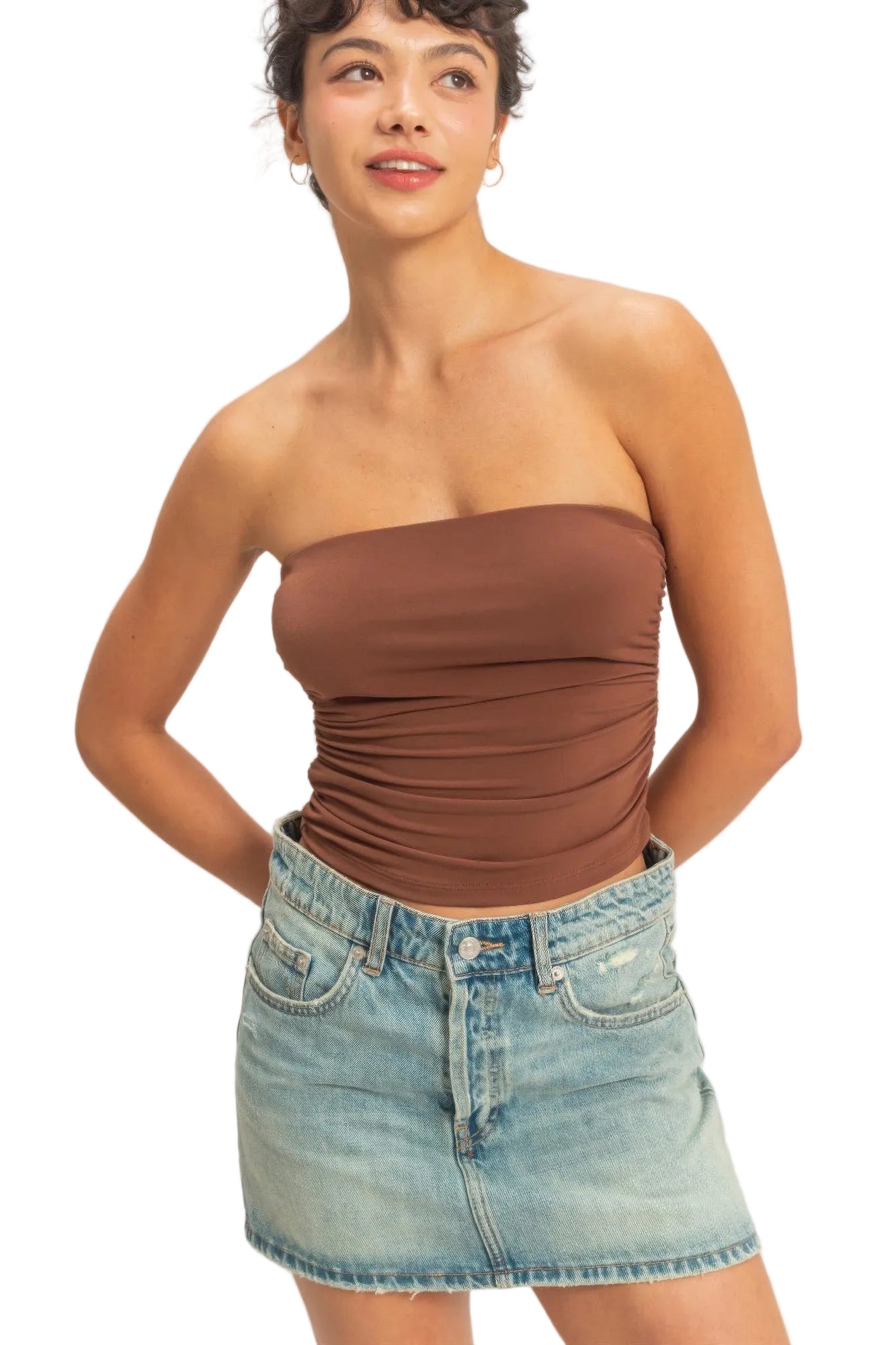 Woman wearing a brown strapless top and denim skirt against a plain background