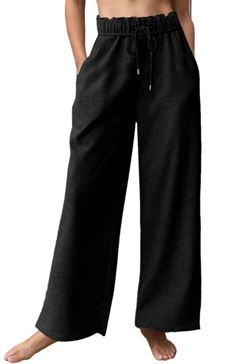 Person wearing black wide-leg pants standing against a neutral wall.