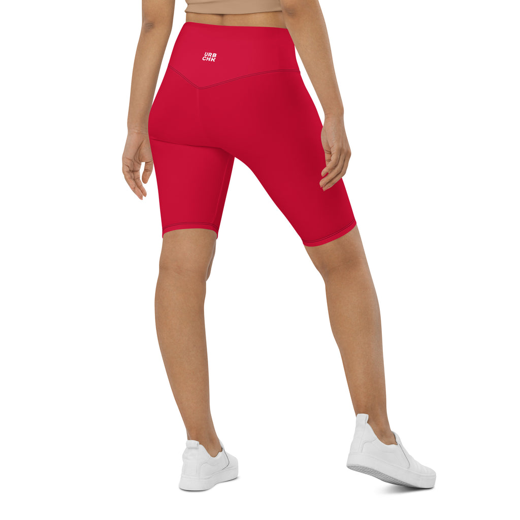 A woman wearing red high-waisted biker shorts with a visible brand logo on the waistband, paired with white sneakers.