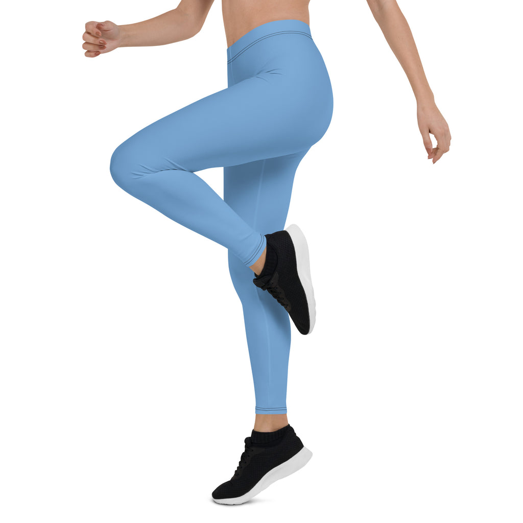 A woman wearing blue mid-rise leggings and black shoes, posing with one leg lifted and ankle flexed.