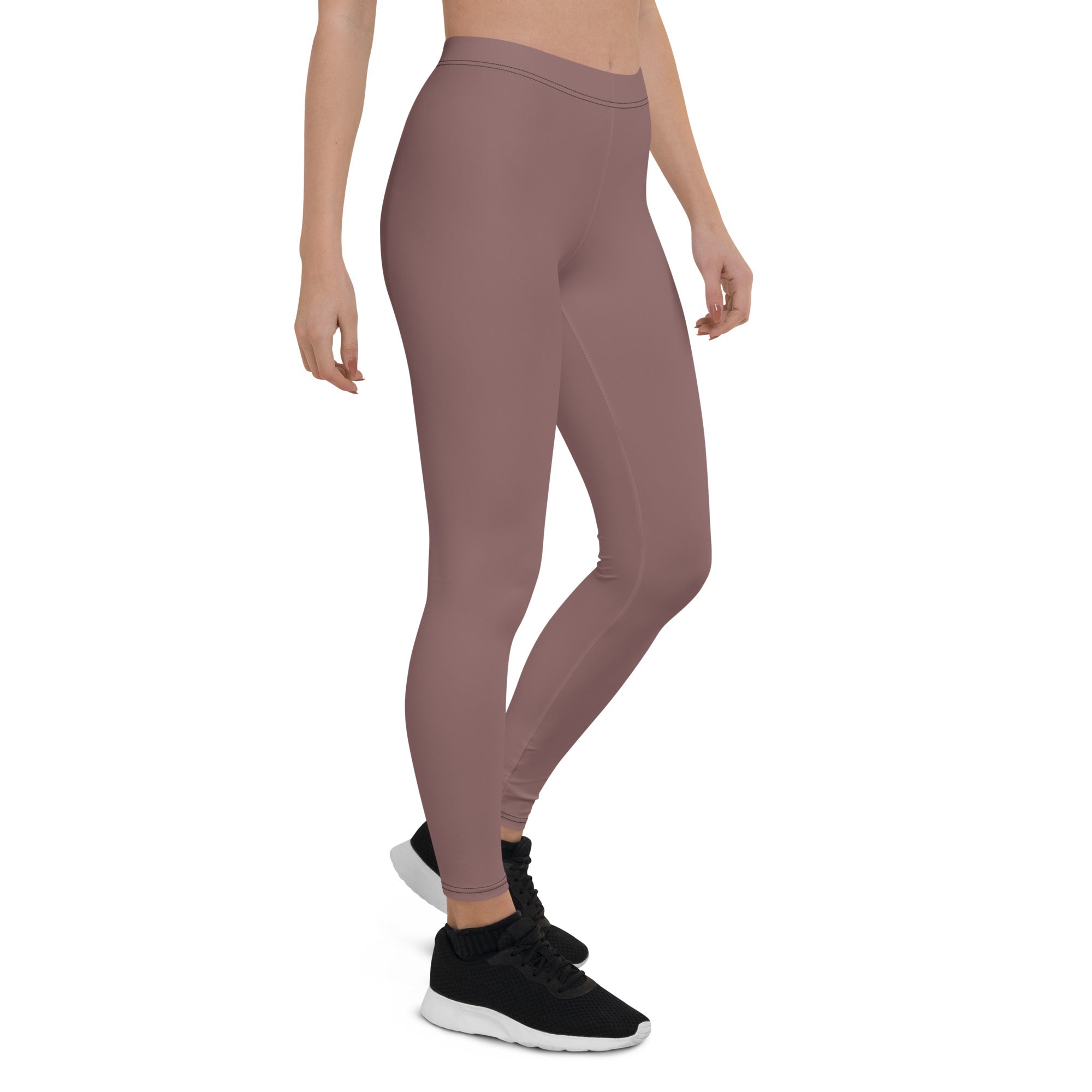 A woman standing wearing mid-rise, solid color leggings and black shoes.