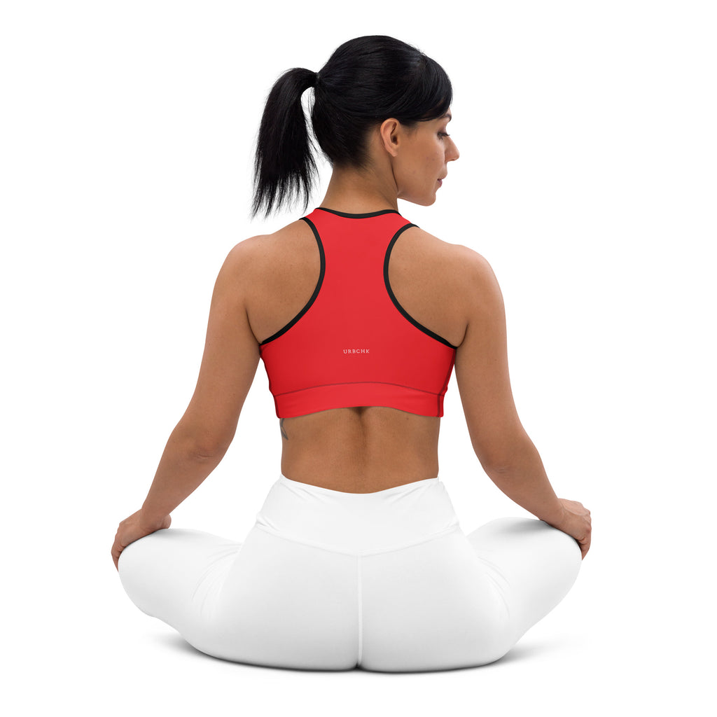 A woman sitting in a kneeling position wearing a red and white sports bra with a scoop neckline and racerback design, with no visible brand marking.