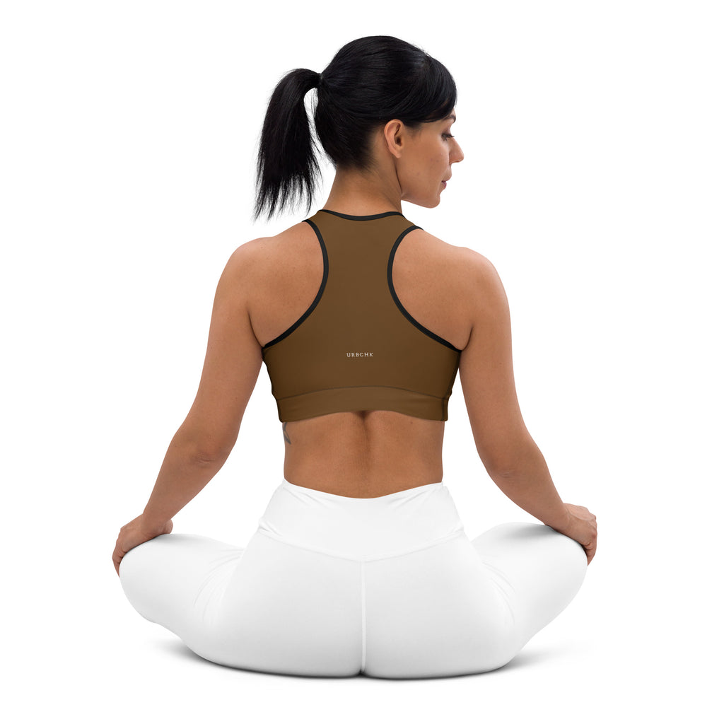 A woman wearing a brown sports workout bra with adjustable straps and removable padding, sitting in a kneeling position.