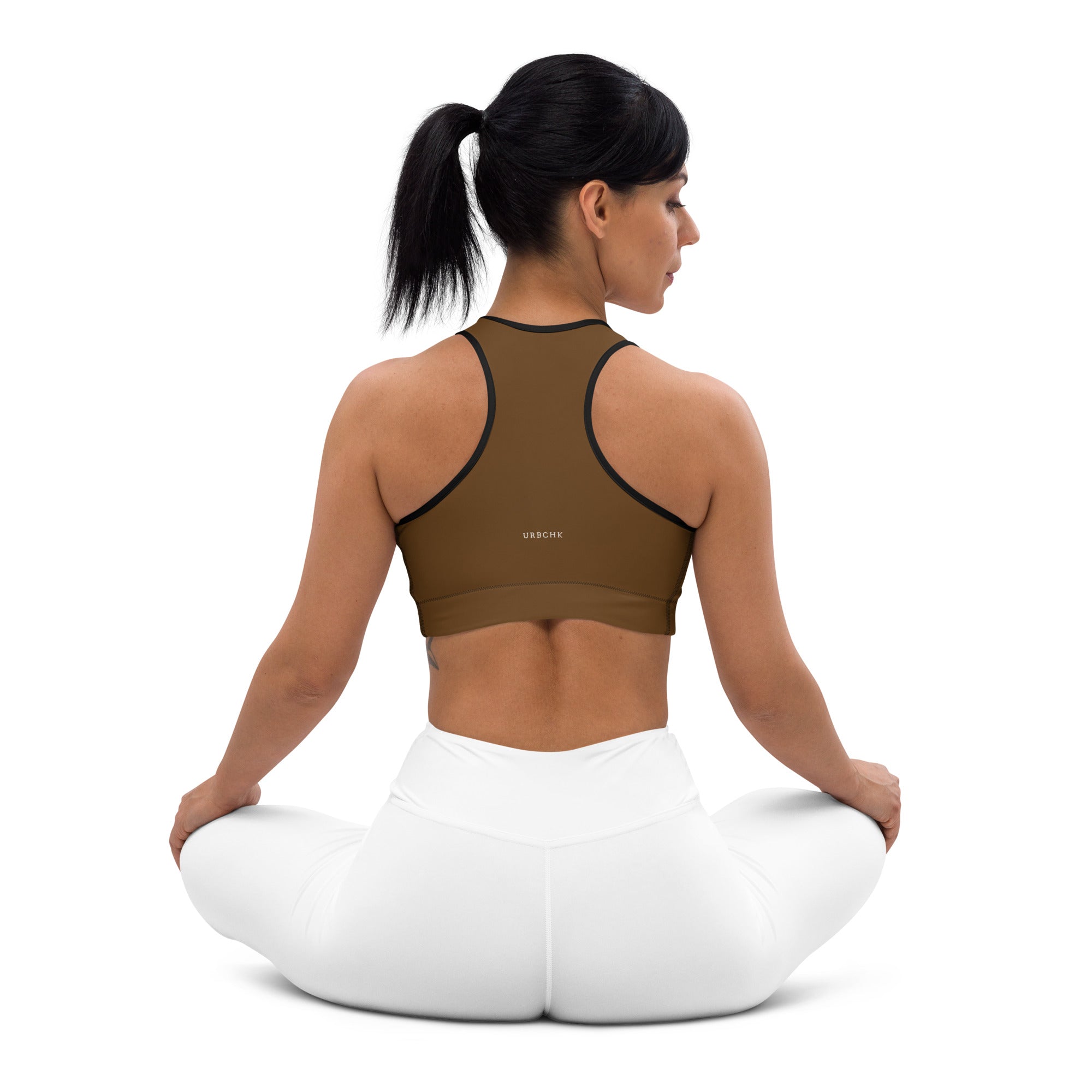 A woman wearing a brown sports workout bra with adjustable straps and removable padding, sitting in a kneeling position.