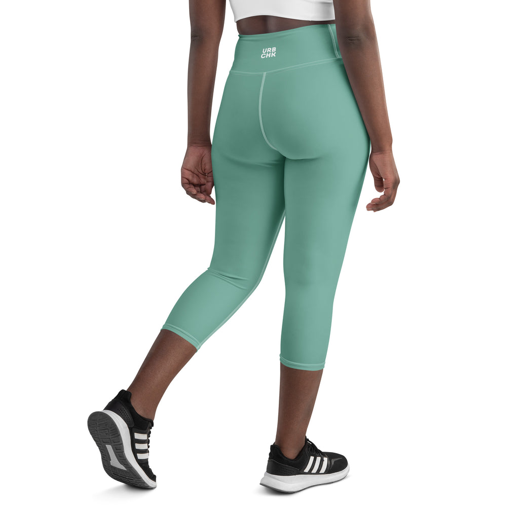A pair of green high waistband capri leggings with a visible brand logo on the waistband, mid-calf length, with the wearer facing sideways.