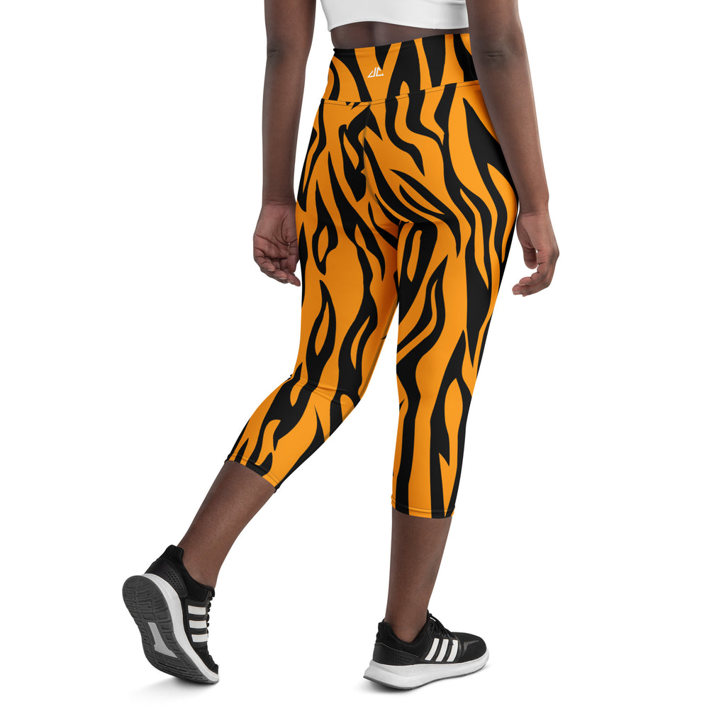 A person wearing orange and black striped capri leggings with a high-waisted fit and an adidas logo on the thigh.