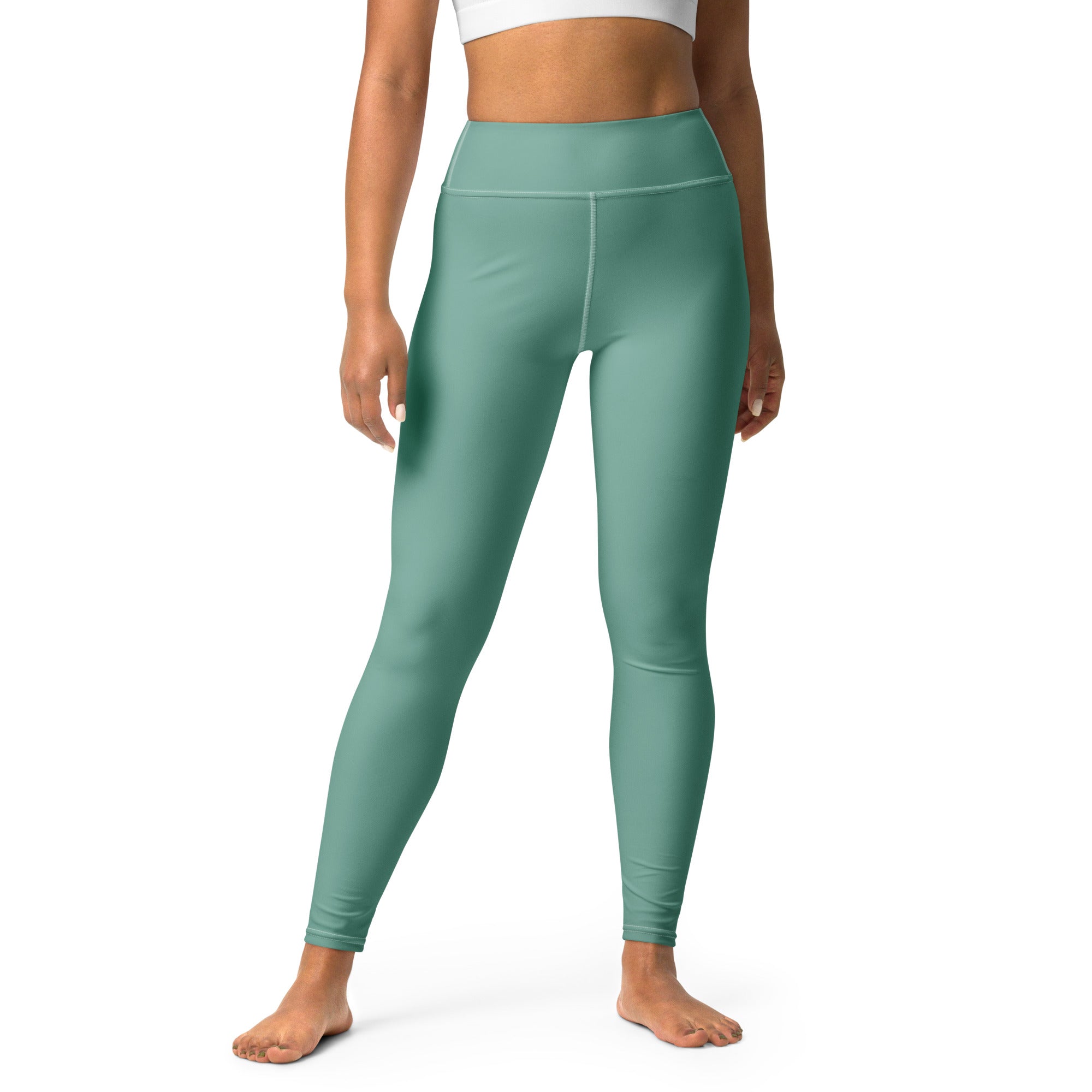A woman standing wearing green high-waisted yoga leggings and a white sports top.
