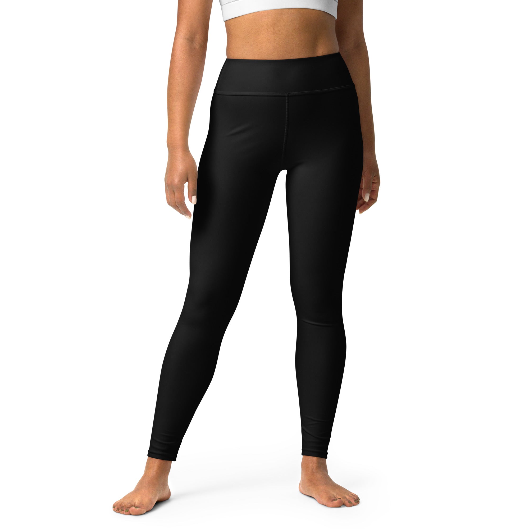 A woman standing wearing black high-waisted yoga leggings and a white sports top.